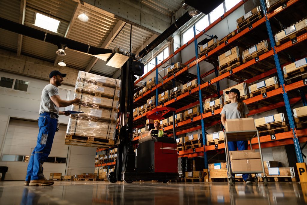 Low angle view of happy warehouse workers communicating while working with shipment in industrial storage compartment.