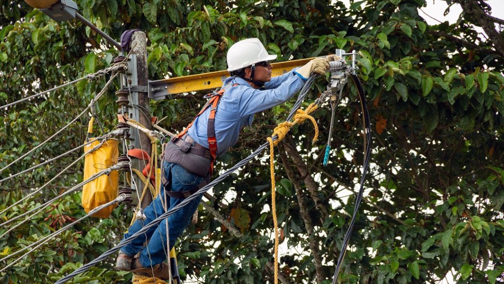 Male electrician working at the height of a pole connecting high voltage power cables. Man using electrical work tool.